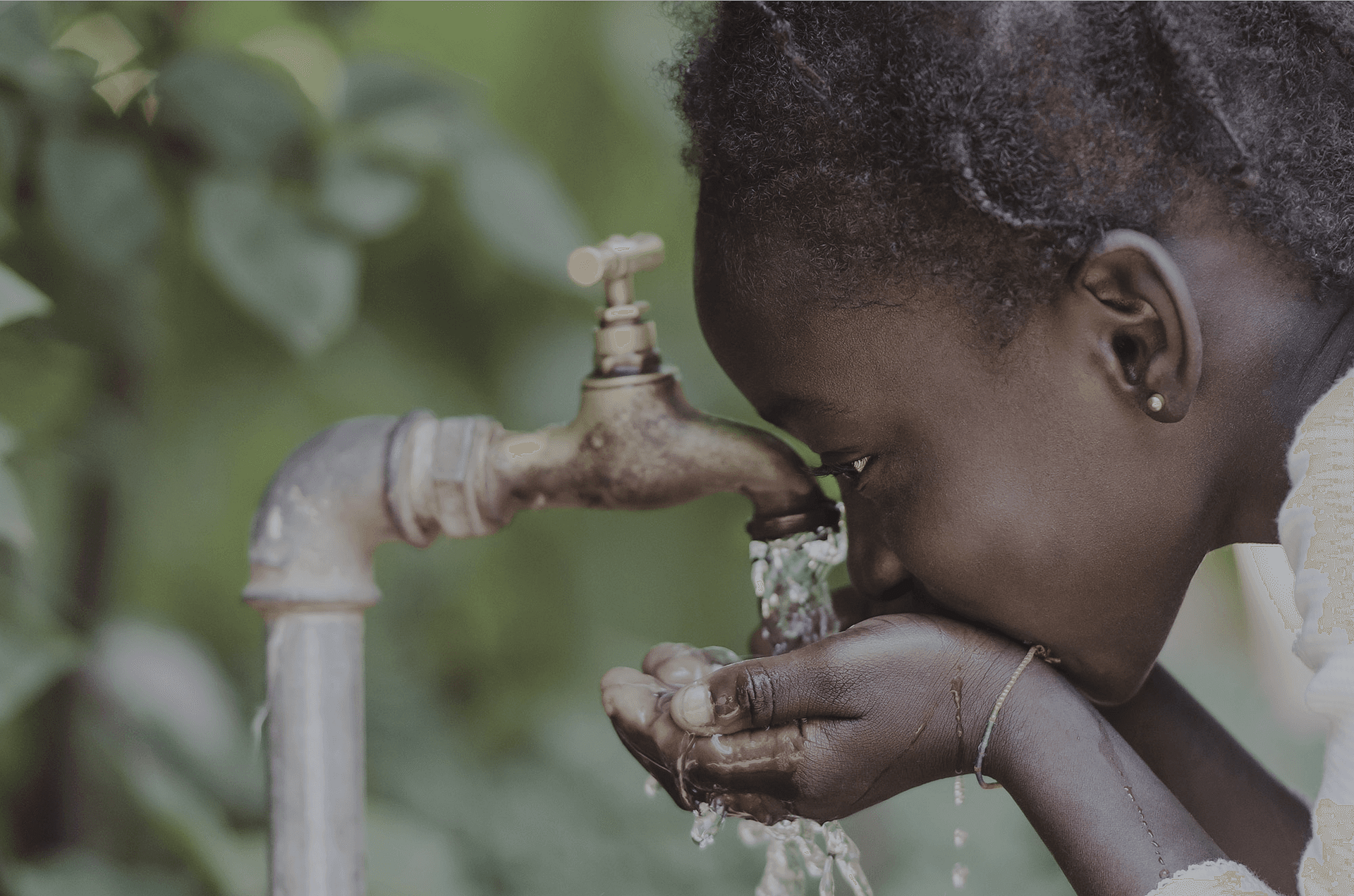 Niña bebiendo agua potable de un grifo, con las manos formando un cuenco.